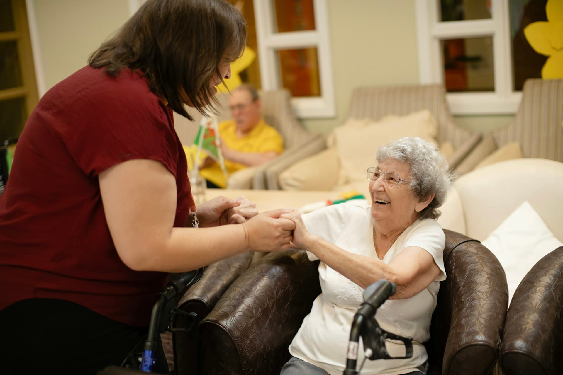 A caregiver holding hands with a smiling resident in a bright, homely care setting